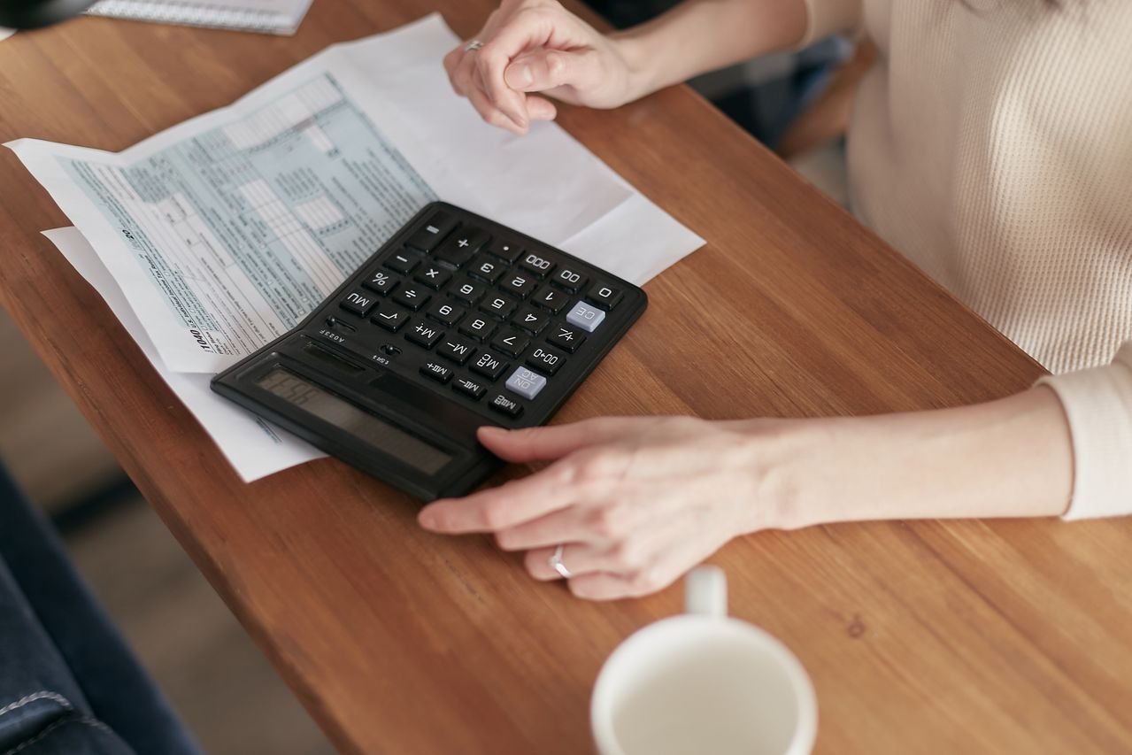 Focused individual using calculator to manage personal finances at wooden desk