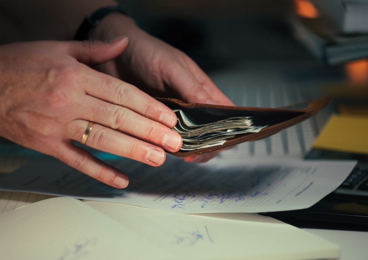 Hands holding an open wallet filled with cash above documents, indicating financial planning or budgeting