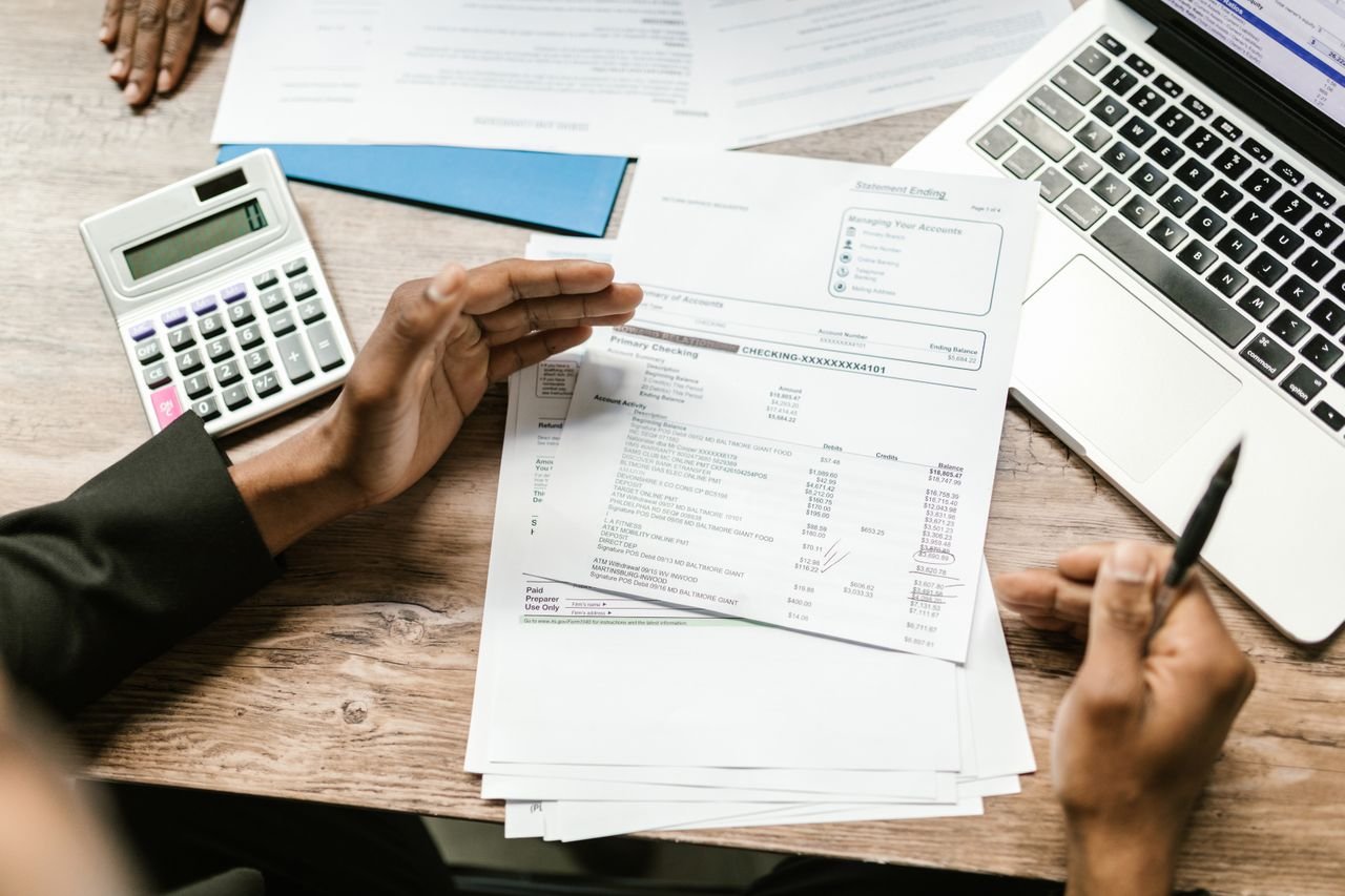 Hands holding financial documents with calculator and laptop on office desk, business analysis scene